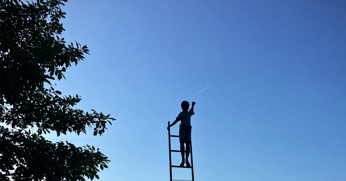 Child on ladder against blue sky signifying growing up and becoming emotionally mature.