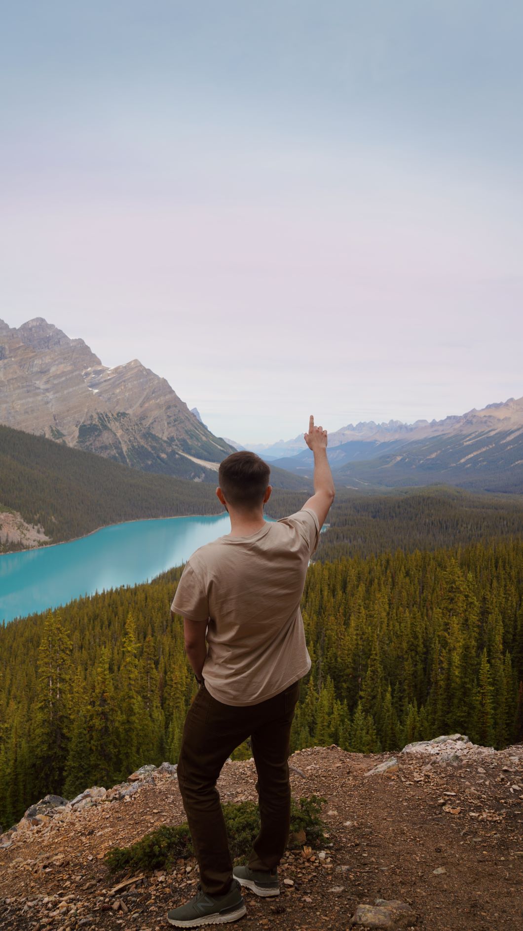 Young man pointing one finger upward as he stands with his back to the viewer looking out on a beautiful blue river and mountains. One word gives us divine direction.