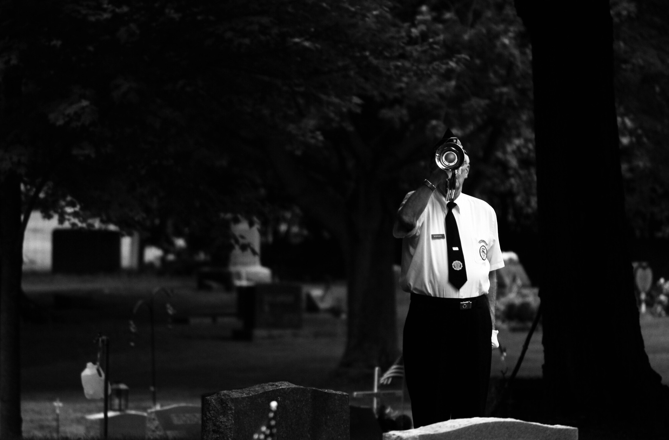 When Sorrow Comes at Christmas is embodied in this black and white photo of a man playing taps on a trumpet in a cemetery at a funeral.